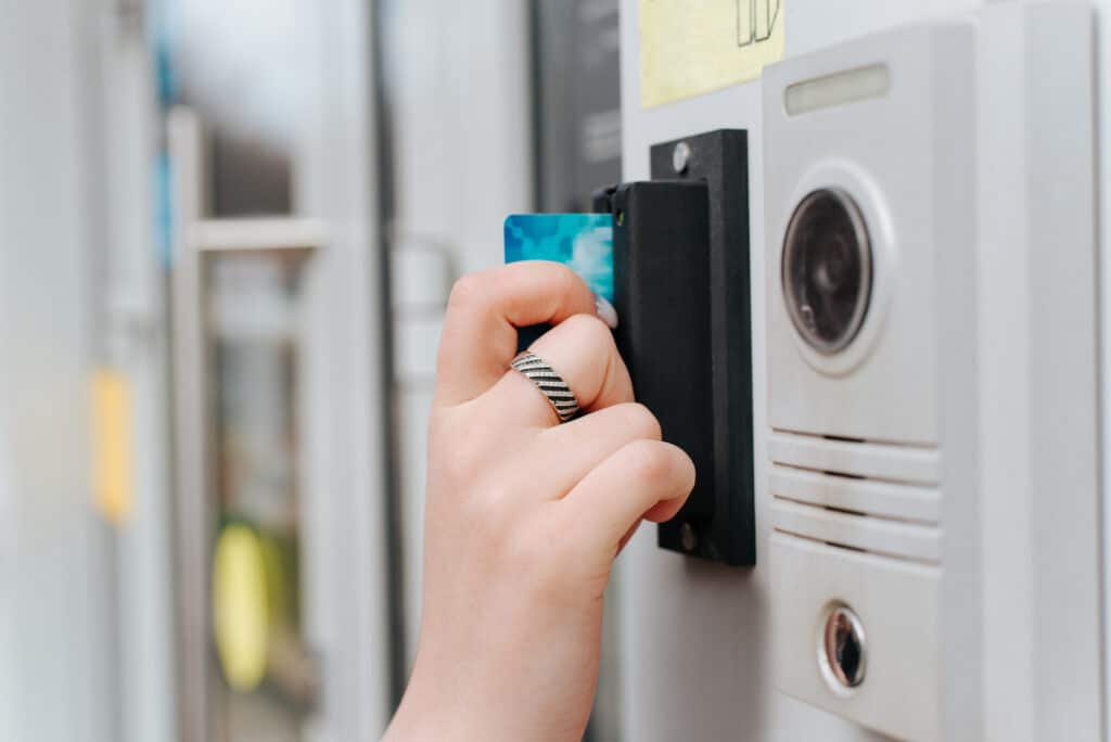 Woman opening door using card entry access system, close up. Side view of woman's hand scanning card through special security equipment, outdoors. Selective focus